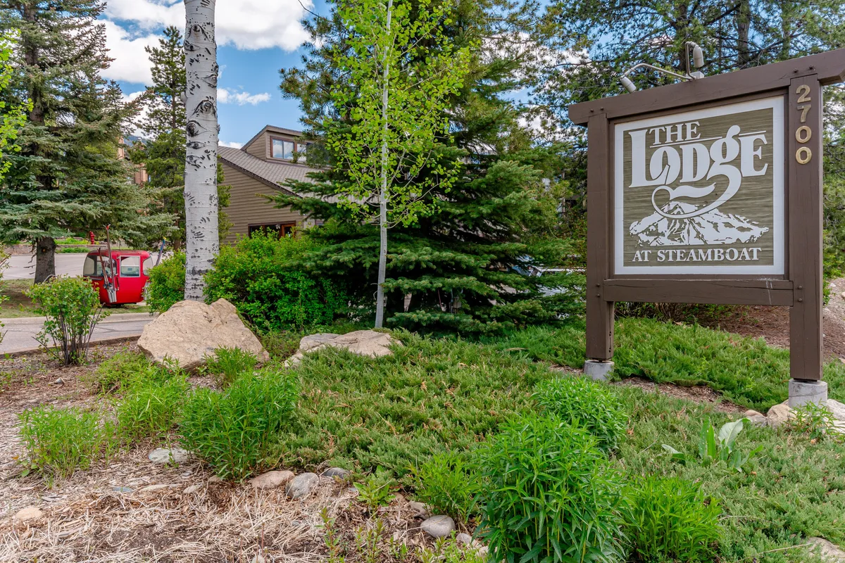 This image shows the exterior of The Lodge, featuring the welcoming sign, lush landscaping, and a red vehicle parked nearby. It exudes a sense of arrival and hints at access to nearby nature and outdoor adventures.