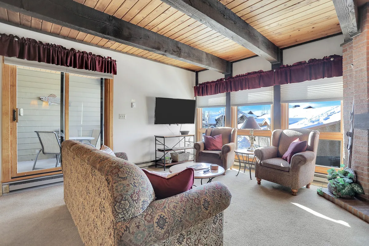 A welcoming living area with a comfortable sofa and armchairs arranged around a television. Large windows let in natural light, offering views of the outdoors and enhancing the space's relaxation potential, ideal for winding down after a day of adventure.
