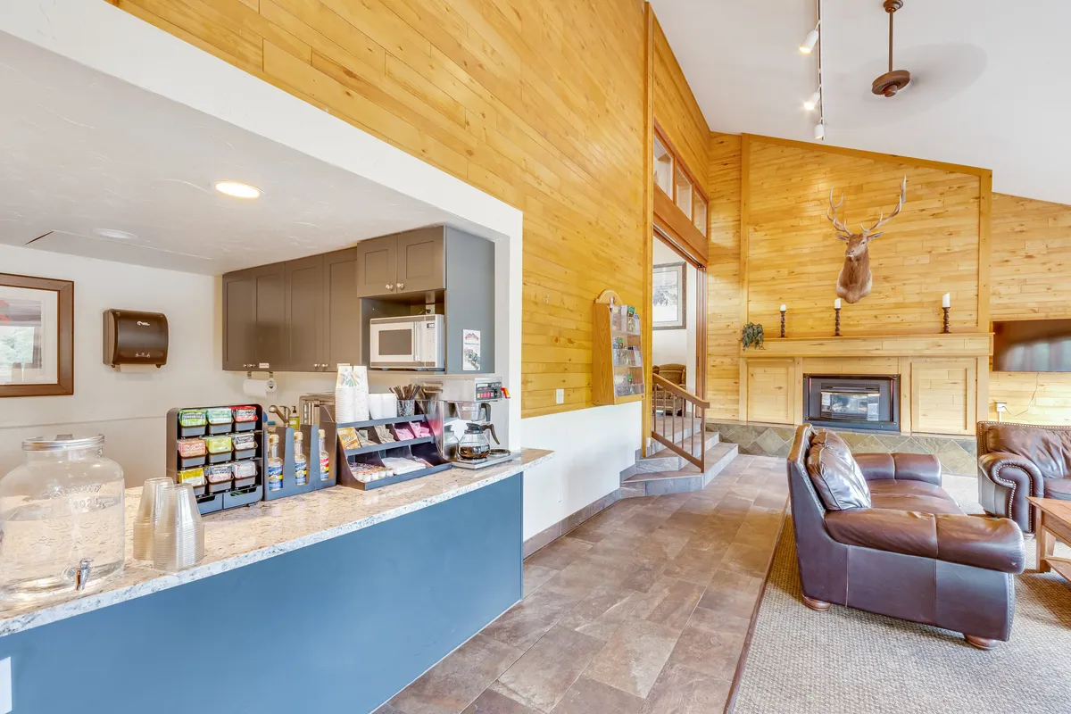 A cozy living space featuring a coffee station, fireplace, leather couch, and wood-paneled walls. The atmosphere is warm and communal, ideal for gathering with friends or family to relax, play games, or enjoy a hot drink after outdoor activities.