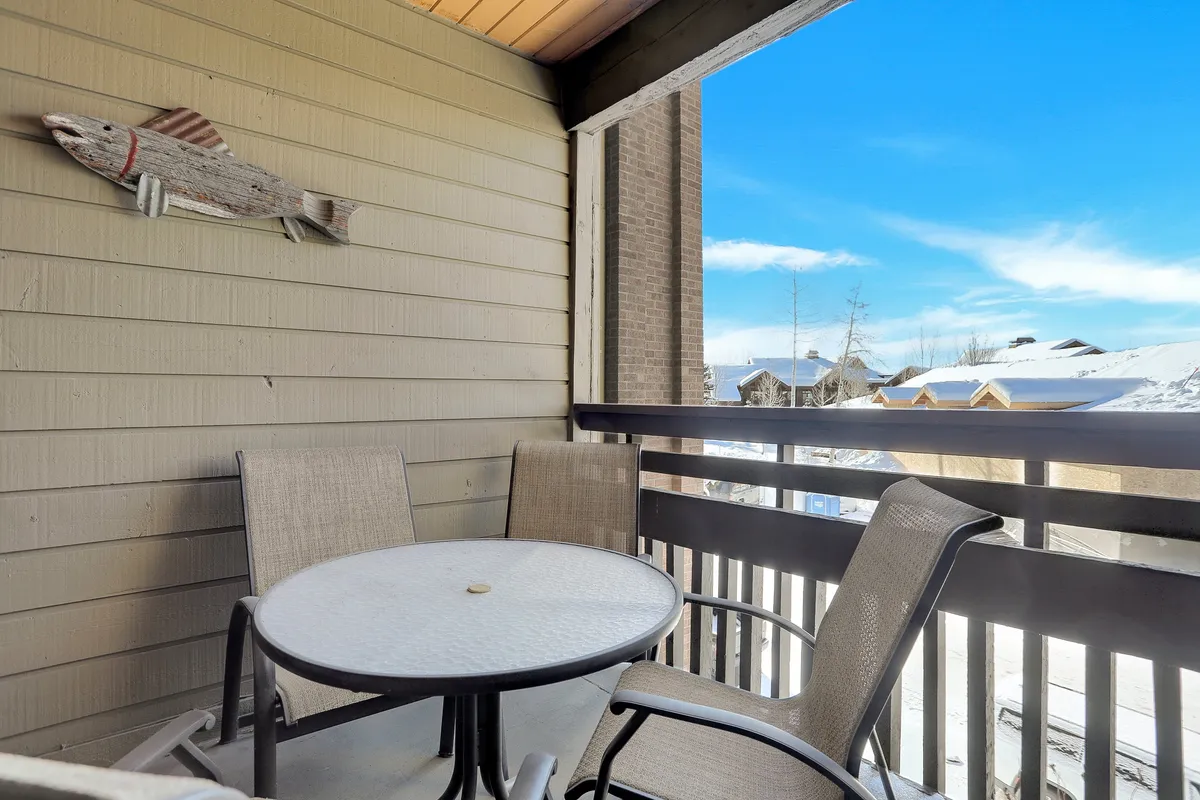 An inviting outdoor seating area set on a balcony or patio, featuring a table and chairs with decorative fish wall art on the exterior wall. The view extends to the surrounding natural landscape, conveying the property's proximity to outdoor activities and the tranquil environment guests can enjoy year-round.