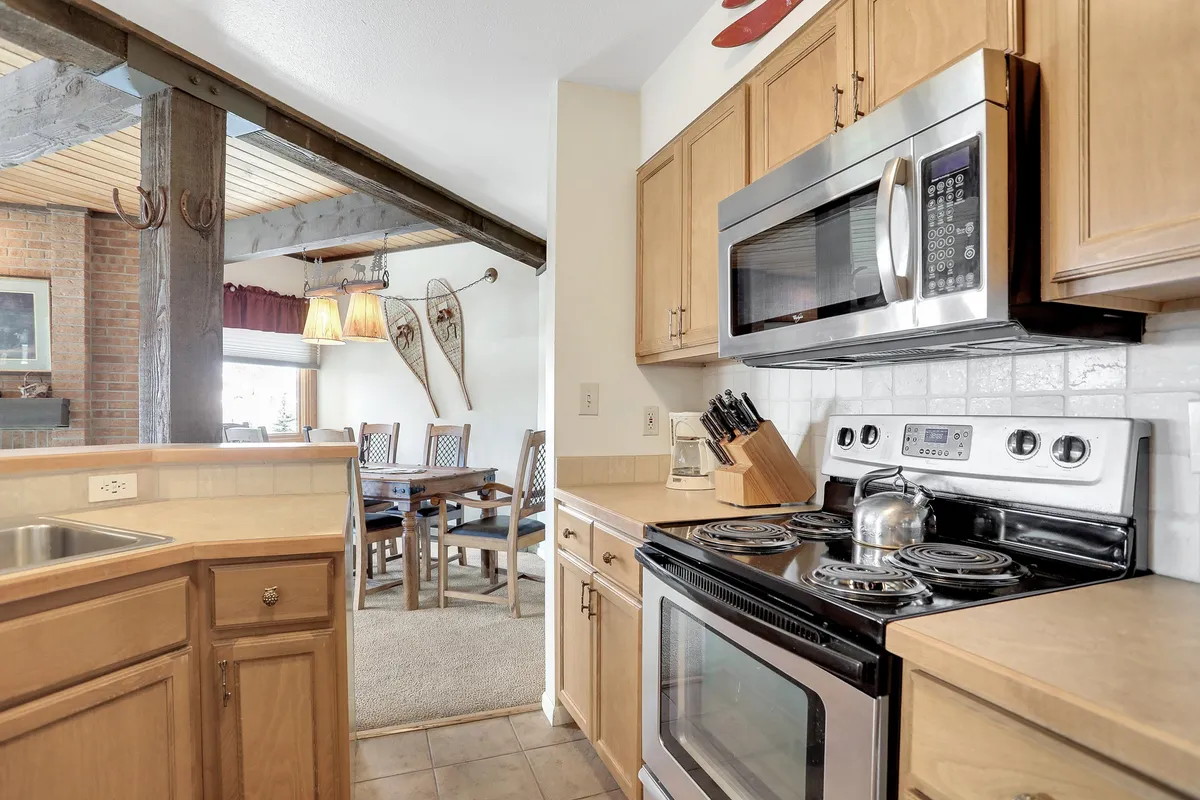 A welcoming view of the condo's kitchen and dining area, featuring stainless steel appliances, wooden cabinetry, a central kitchen island, and the dining area visible in the background. The space feels spacious, functional, and perfect for both cooking and gathering.