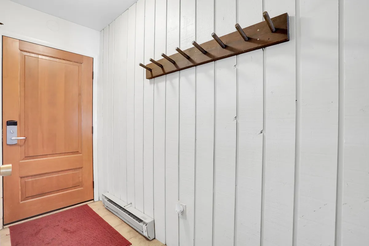 A welcoming entryway with a front door, coat rack, and a vibrant red rug. The space suggests the transition from outdoor explorations to the comforts of home, highlighting the anticipation of returning to a cozy environment after engaging in seasonal adventures.