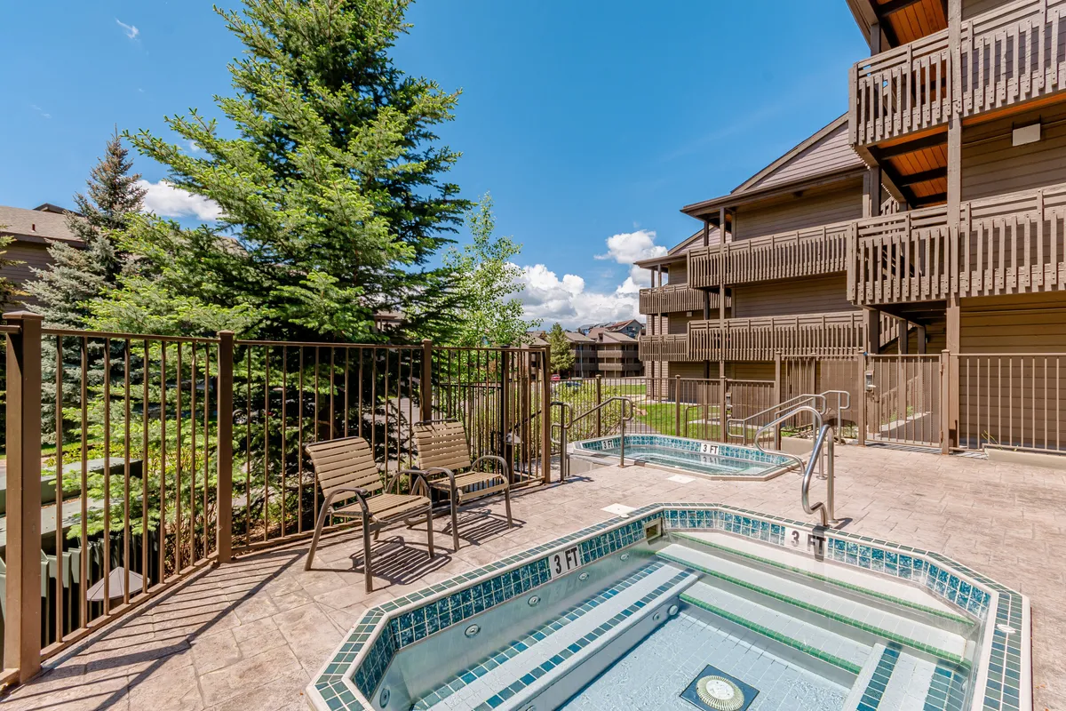 An inviting outdoor area featuring multiple bubbling hot tubs, surrounded by lush greenery and comfortable patio furniture. The relaxed atmosphere encourages socializing or quiet moments in nature, embodying the communal, resort-like amenities.