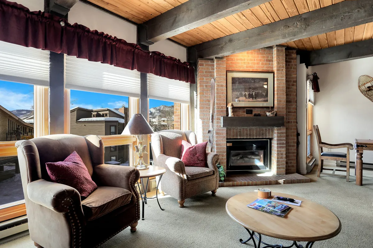 A cozy living area anchored by a brick fireplace, with comfortable seating arranged for relaxation and large windows that fill the room with natural light. The coffee table and accessories create an inviting atmosphere for reading, socializing, or unwinding.